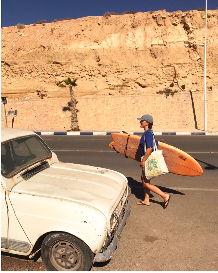 kvinne går langs vei med oransje surfebrett